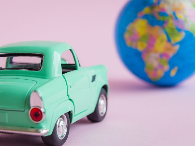 Een groene speelgoedauto staat naast een wereldbol, wat irritaties oproept, op een roze achtergrond.