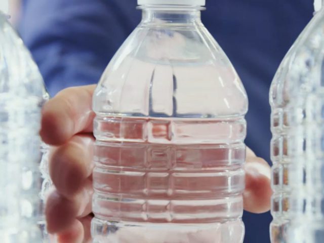 Een man houdt verschillende plastic flessen gevuld met water vast.