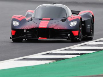 Een rode en zwarte Aston Martin Valkyrie-raceauto op een circuit.