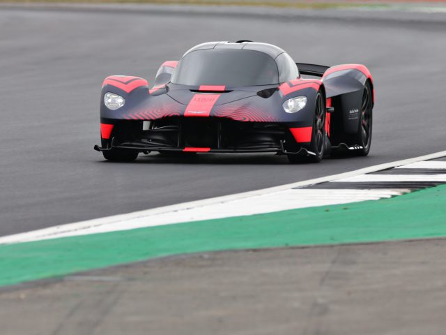Een Aston Martin Valkyrie, zwart en rood, racet op een circuit.