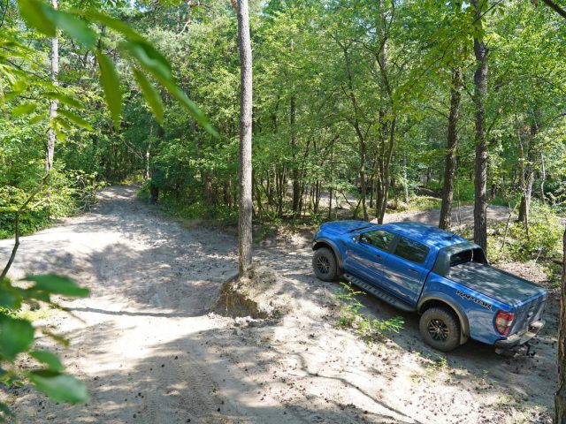 Een blauwe vrachtwagen, rechtstreeks uit Fast & Furious: Hobbs & Shaw, rijdt over een onverharde weg in het bos.
