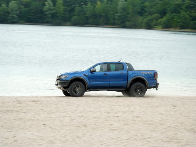 Een blauwe Ford Ranger rijdt snel op een zandstrand.