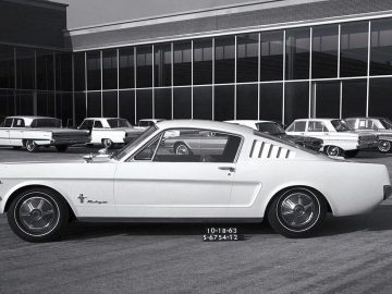 Een zwart-witfoto van een Mustang geparkeerd voor een gebouw.