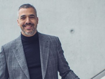 Een man in een grijs pak glimlacht terwijl hij op de Mitsubishi-trap staat.