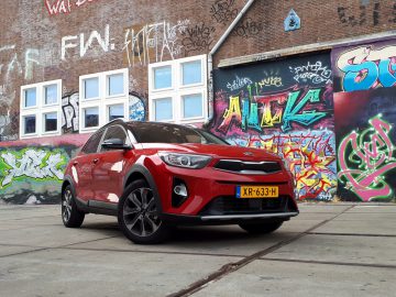Een rode Kia Stonic geparkeerd voor een met graffiti bedekte muur.