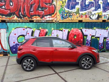 Een rode Kia Stonic geparkeerd voor een met graffiti bedekt gebouw.