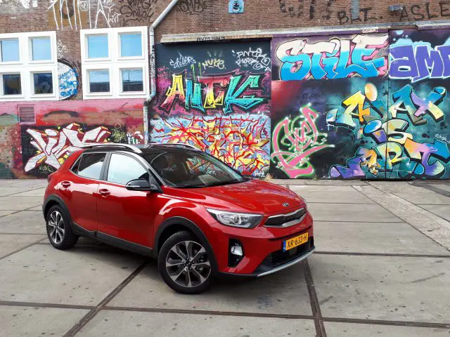 Een rode Kia Stonic geparkeerd voor een met graffiti bedekte muur.