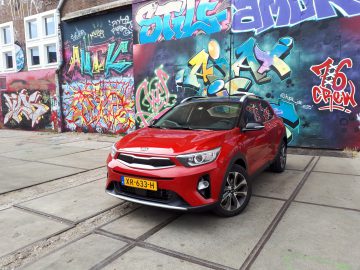 Een rode Kia Stonic geparkeerd voor een met graffiti bedekte muur.