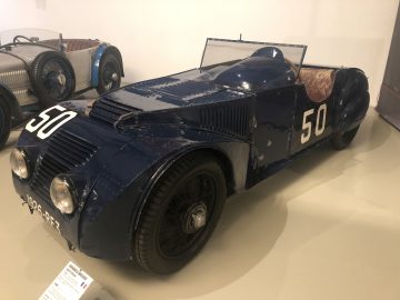 Een blauwe vintage Le Mans-auto staat tentoongesteld in een museum.