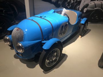 In een museum staat een blauwe Le Mans-raceauto tentoongesteld.