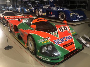 Een groen-oranje Le Mans-raceauto staat tentoongesteld in een museum.