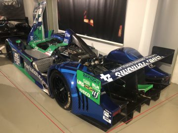 Een blauw-groene racewagen van Le Mans is te zien in een museum.