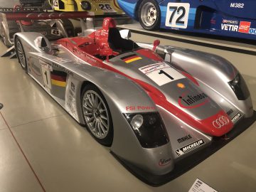 Een zilveren Le Mans-raceauto tentoongesteld in een museum.