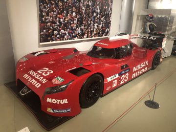 In een museum staat een rode Le Mans-raceauto tentoongesteld.