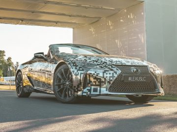 Een gecamoufleerde Lexus-sportwagen staat geparkeerd voor een gebouw.