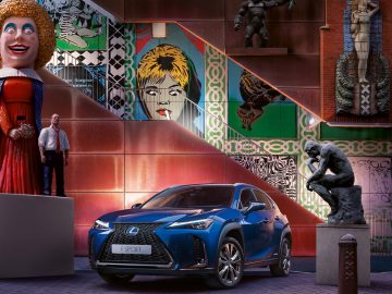 Een blauwe Lexus CX SUV voor een standbeeld tijdens een stedelijke kunsttour.