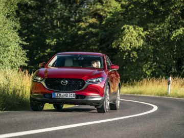De rode Mazda 3 uit 2019 rijdt over een landweg.