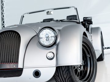 Een zilveren Morgan Plus 4-sportwagen staat geparkeerd in een kamer.