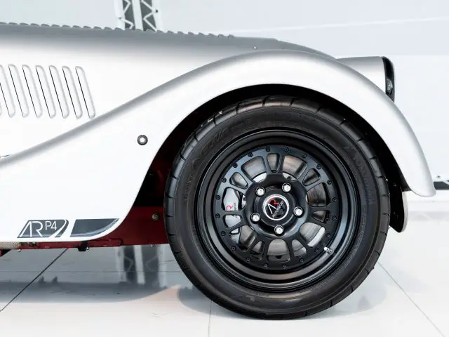 In een witte kamer wordt een zilveren Morgan Plus 4-sportwagen getoond.