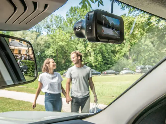 Een man en een vrouw staan met een dashcam voor een auto.