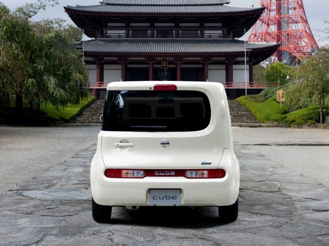 Een witte Nissan Cube geparkeerd voor een pagode.