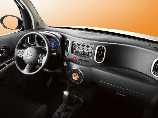 Het interieur van een kleine Nissan Cube met dashboard en stuur.