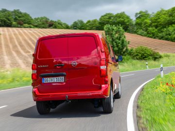 Een rode Opel Vivaro rijdt over een landweg.