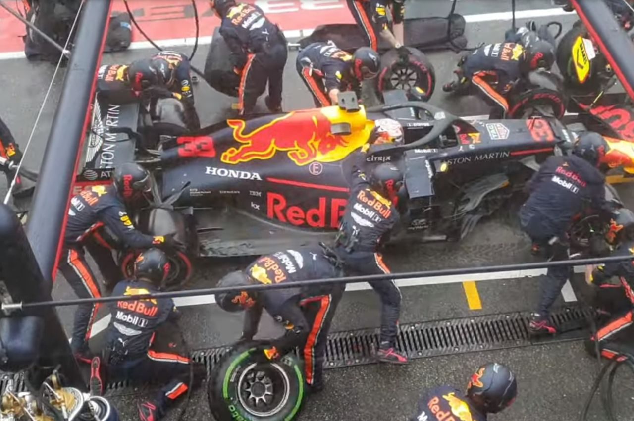 Een groep Red Bull Racing-coureurs, waaronder Max Verstappen, werkt aan hun auto.