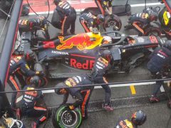 Een groep Red Bull Racing-coureurs, waaronder Max Verstappen, werkt aan hun auto.