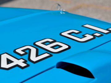 Op de motorkap van een blauwe sportwagen staat een nummer, verborgen door een sluier.