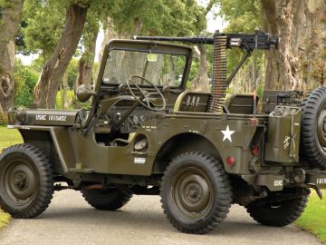 In een bosrijke omgeving staat een oude militaire jeep met een jerrycan eraan vast.