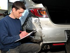 Een man schrijft op een klembord naast een beschadigde auto voor autoverzekeringsdoeleinden.