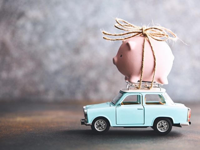 Een spaarvarken bovenop een autoverzekering speelgoedauto.