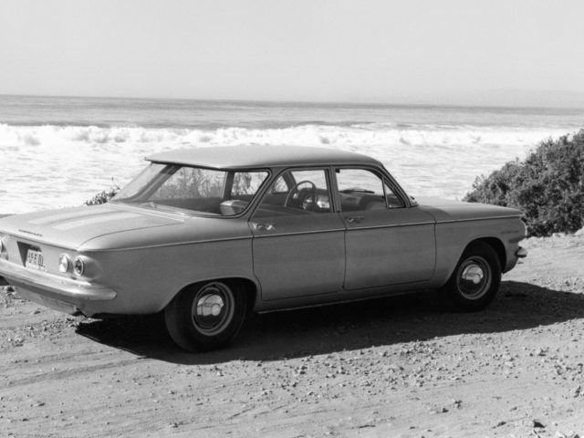 Een zwart-witfoto van een oude Chevrolet Corvair geparkeerd op het strand.