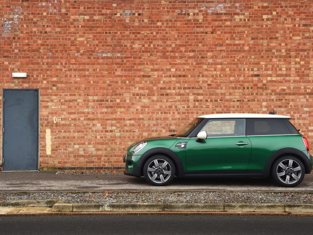 Een groene MINI Cooper S geparkeerd voor een bakstenen muur.