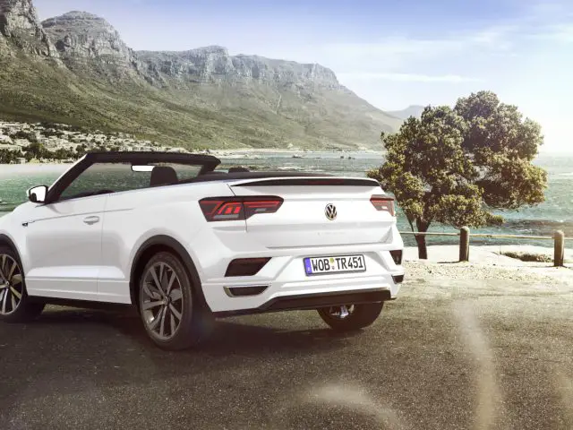 De witte Volkswagen T-Roc Cabrio staat geparkeerd voor de oceaan.