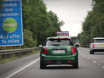 Een groene MINI Cooper S rijdt met een bord over de weg.