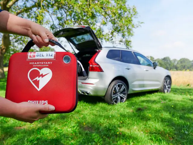 Een persoon met een rode EHBO-doos met een AED voor een auto.