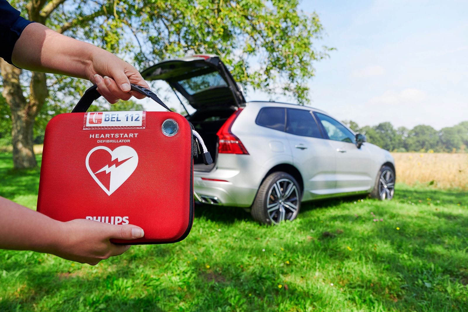 Een persoon met een rode EHBO-doos met een AED voor een auto.