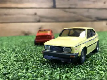 Een gele speelgoedauto Skoda Rapid Coupé staat geparkeerd op groen gras.