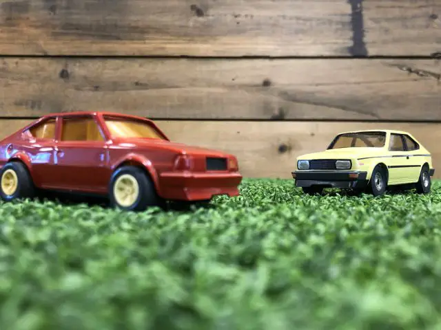 Twee Skoda Rapid Coupé-speelgoedauto's geparkeerd op gras naast elkaar.