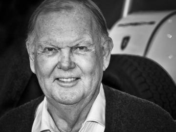 Een zwart-witfoto van een oudere man voor een Porsche.