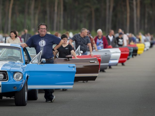 Een groep mensen staat naast een rij Ford Mustangs.