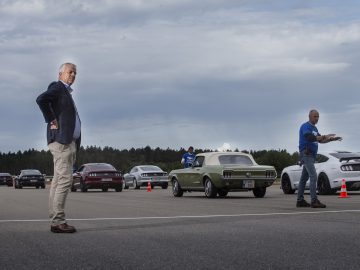 Een man staat naast een Ford Mustang en een groep auto's op een parkeerplaats.