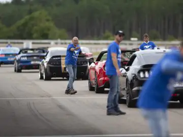 Een groep mannen in blauwe t-shirts staat in een rij Ford Mustang-auto's.