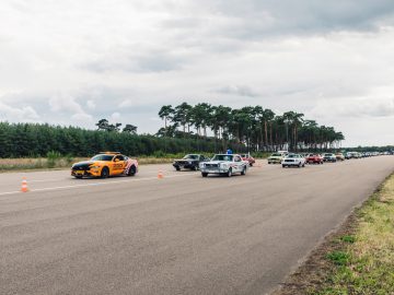Een groep Ford Mustangs rijdt over een weg met kegels op de achtergrond.