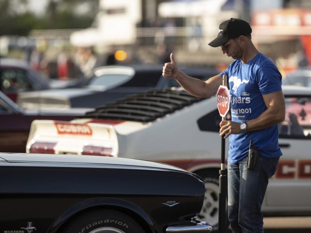 Een man die naast een Ford Mustang staat met een duim omhoog.