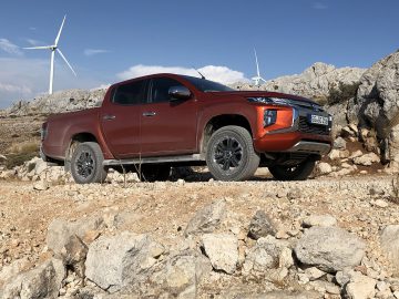 Een rode Mitsubishi L200 geparkeerd voor windturbines.