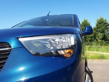 De koplamp van een blauwe Opel Combo Tour geparkeerd op een parkeerplaats.