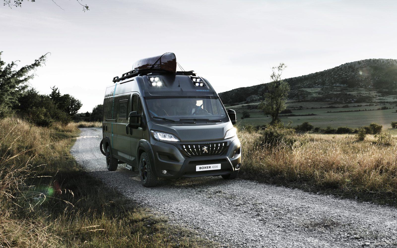 Een zwarte Peugeot Boxer rijdt over een onverharde weg.
